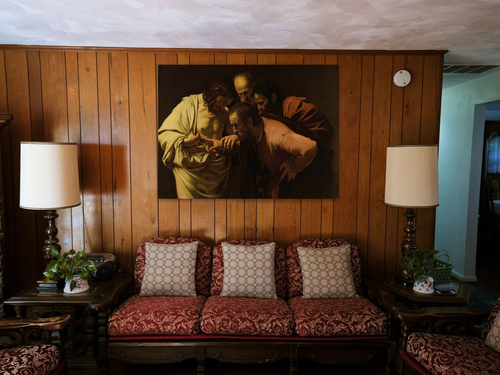 A wood-panelled study with a red patterned sofa between two lamps; above it Caravaggio&rsquo;s The Incredulity of St Thomas, printed at 40 by 60 inches