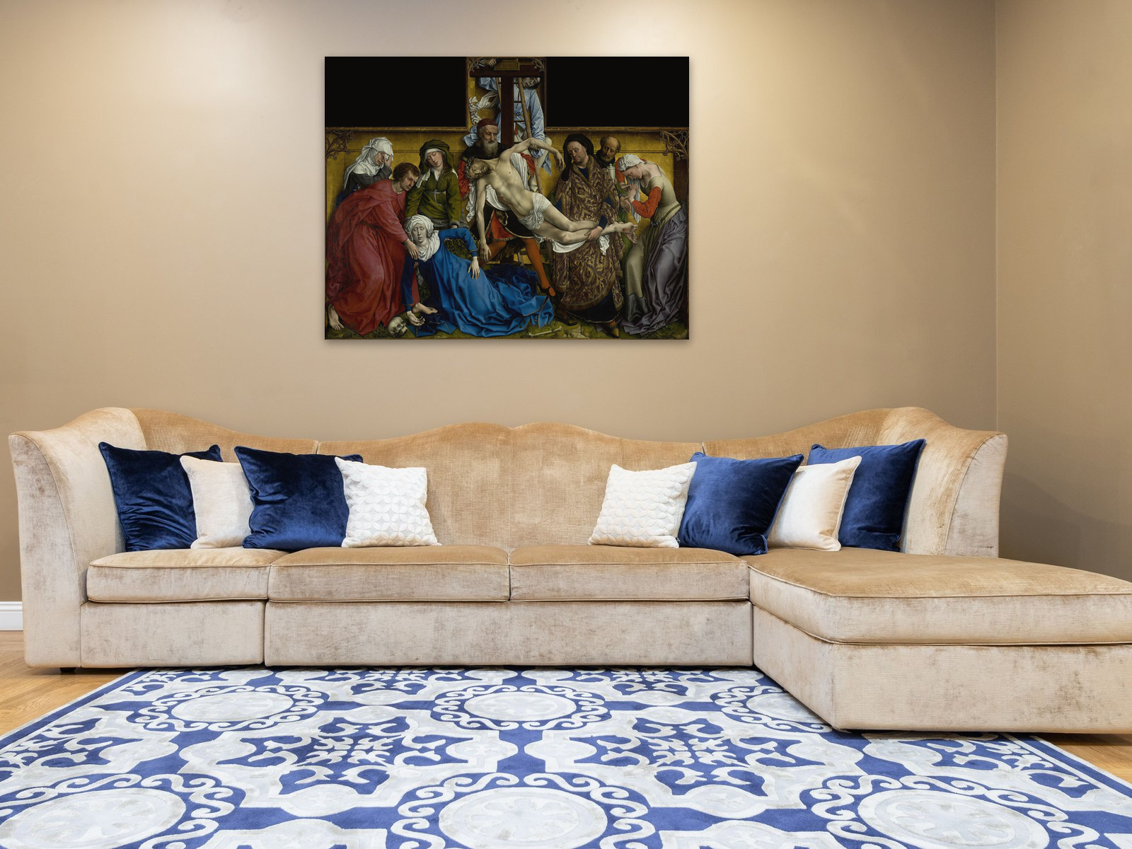 A velvet sectional sofa with blue and cream cushions against a warm beige wall; above it The Descent from the Cross by Rogier van der Weyden, printed at 40 by 60 inches